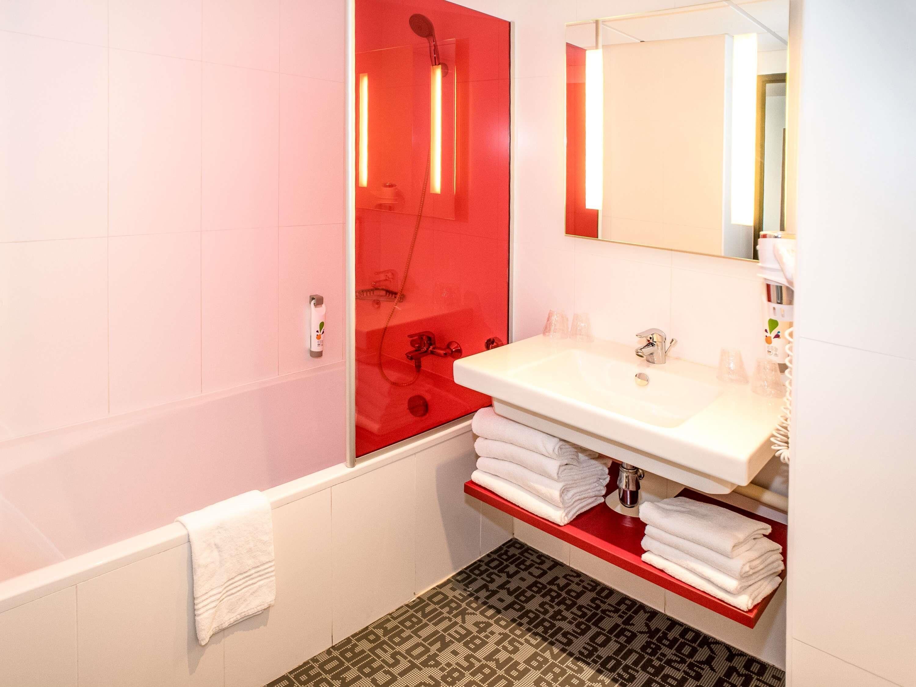 Un baño moderno con una bañera blanca, un box de ducha rojo y un lavamanos blanco con encimera roja.