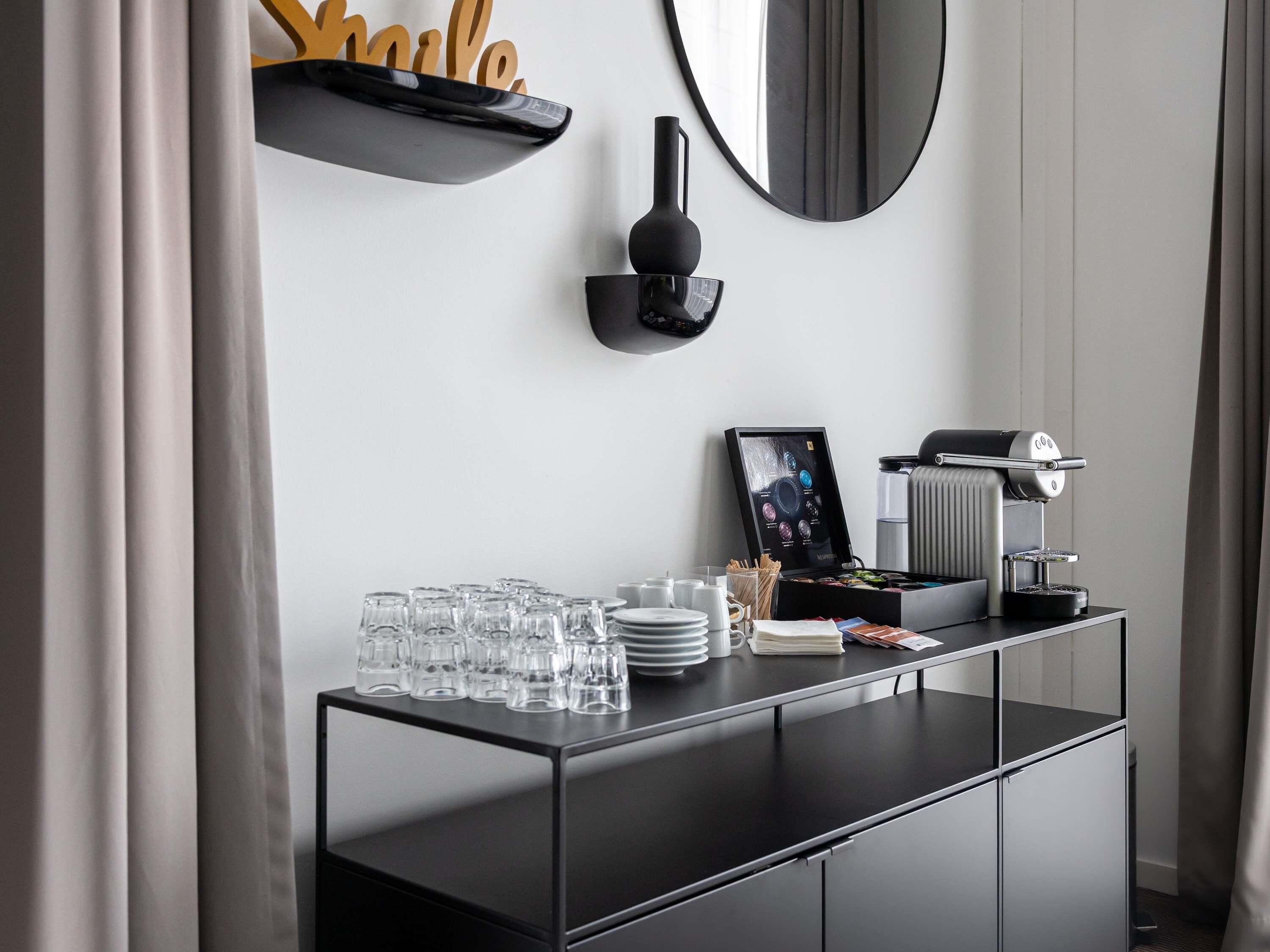 Een moderne hotelkamer met een zwarte console tafel, een koffieapparaat, een inlijsting foto en een spiegel aan de muur.