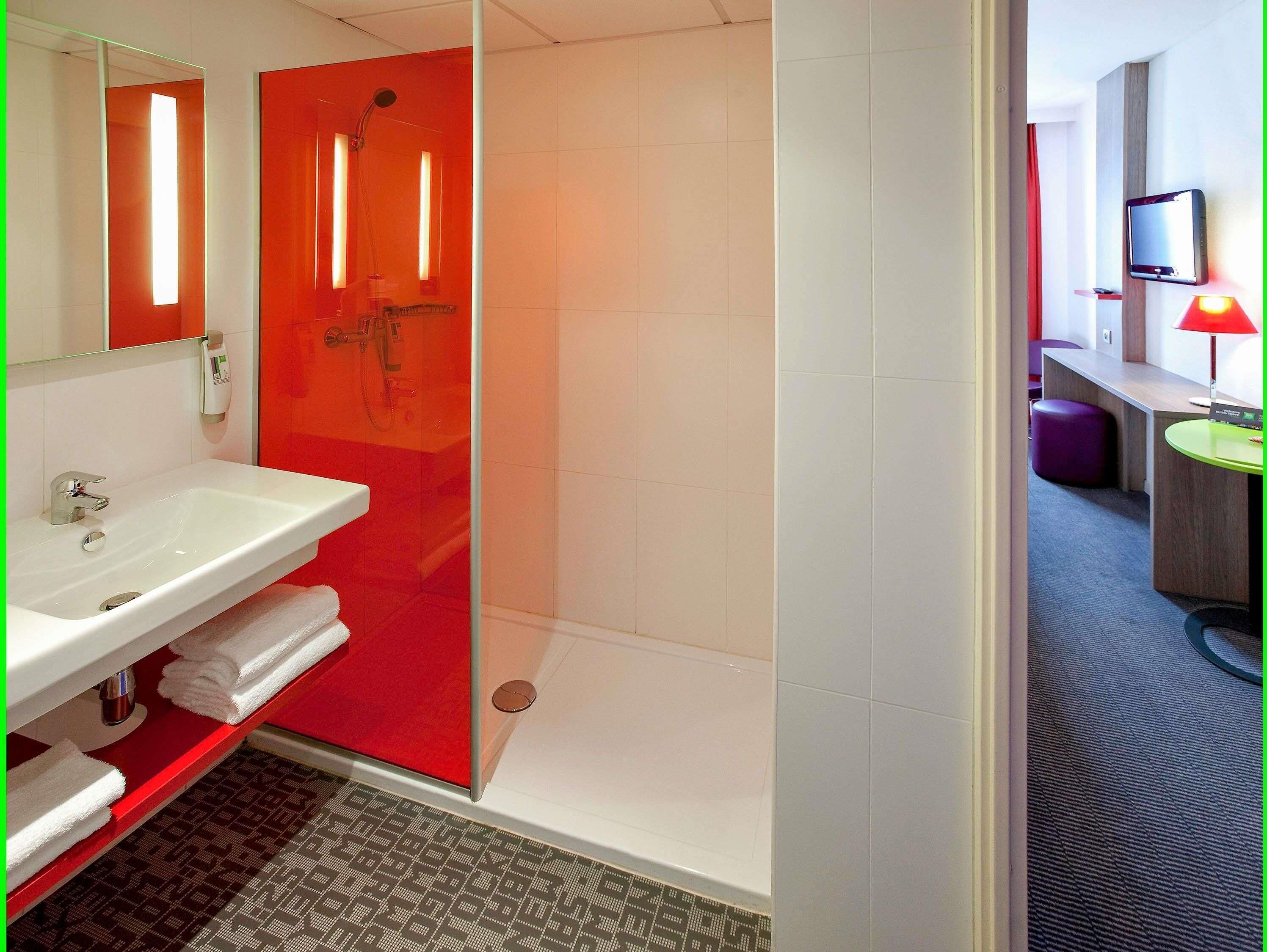 A modern bathroom with a white sink, red accents, and a glass shower enclosure.