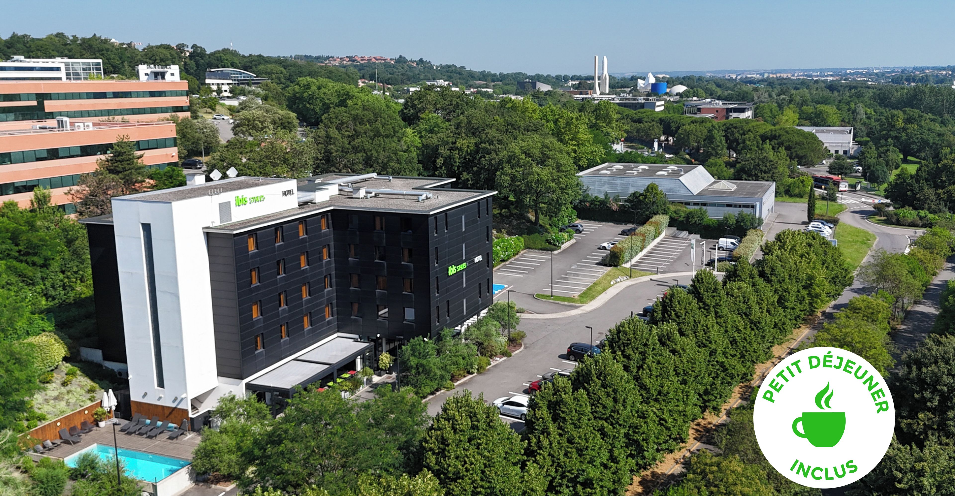 A modern hotel with a rooftop pool, surrounded by lush greenery and a parking area.