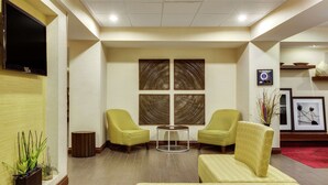 Un hall de hotel con dos sillones amarillos, una mesita redonda y un sofá.