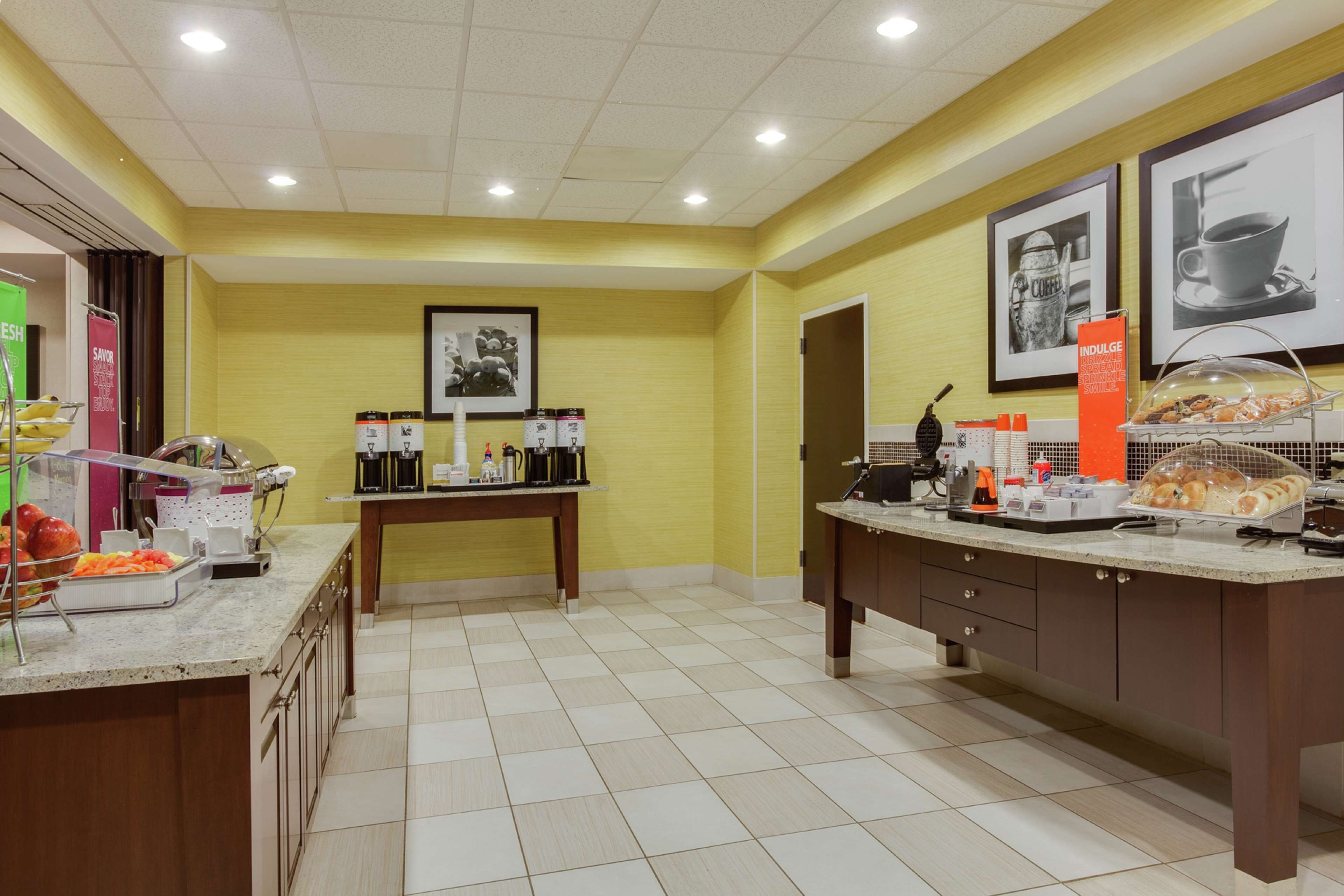 A hotel breakfast area with a buffet setup, including a variety of food items and beverages, and a coffee station.