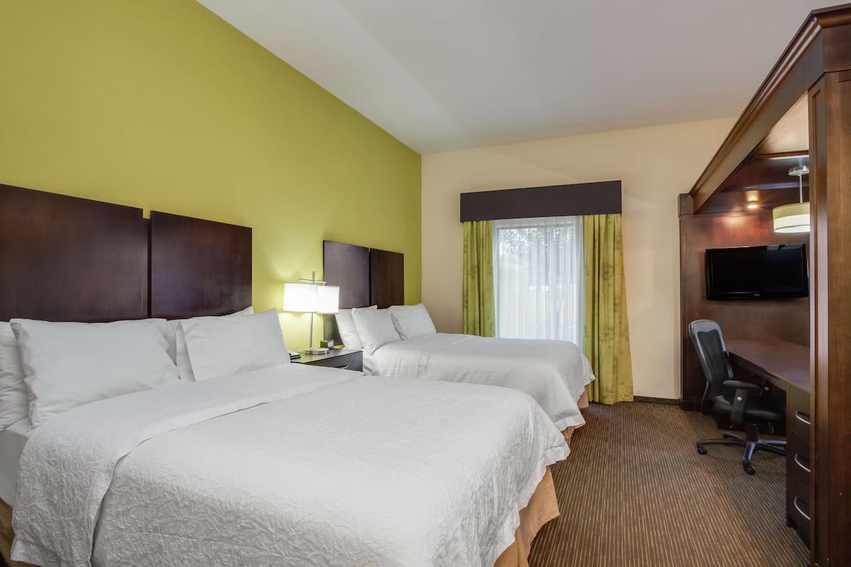 A hotel room with two beds, a desk with a chair, a TV, and a window with curtains.