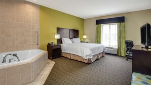 Habitación de hotel con una bañera grande, cama con ropa blanca, escritorio con televisor y ventana con cortinas.