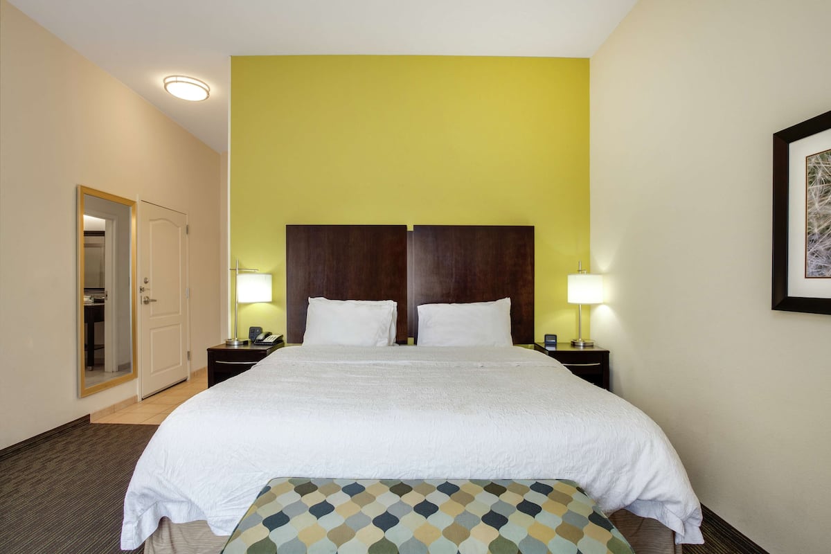 A hotel room with a large bed, two bedside tables with lamps, a door to a bathroom, and a framed picture on the wall.