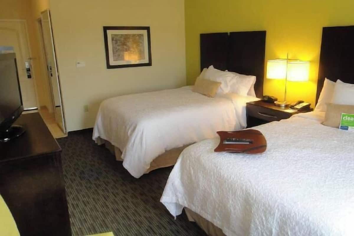 A hotel room with two beds, a desk with a computer, a lamp, and a framed picture on the wall.