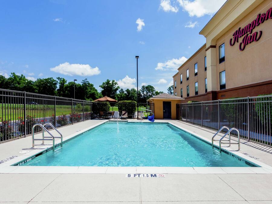 A swimming pool with a fence, a building with 'Hampton Inn' signage, and a clear blue sky.