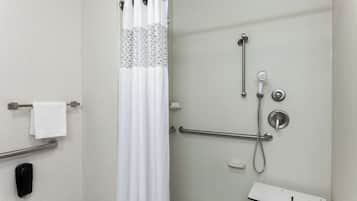 A shower area with a glass door, a white shower curtain, a handheld showerhead, a handheld shower nozzle, and a grab bar.