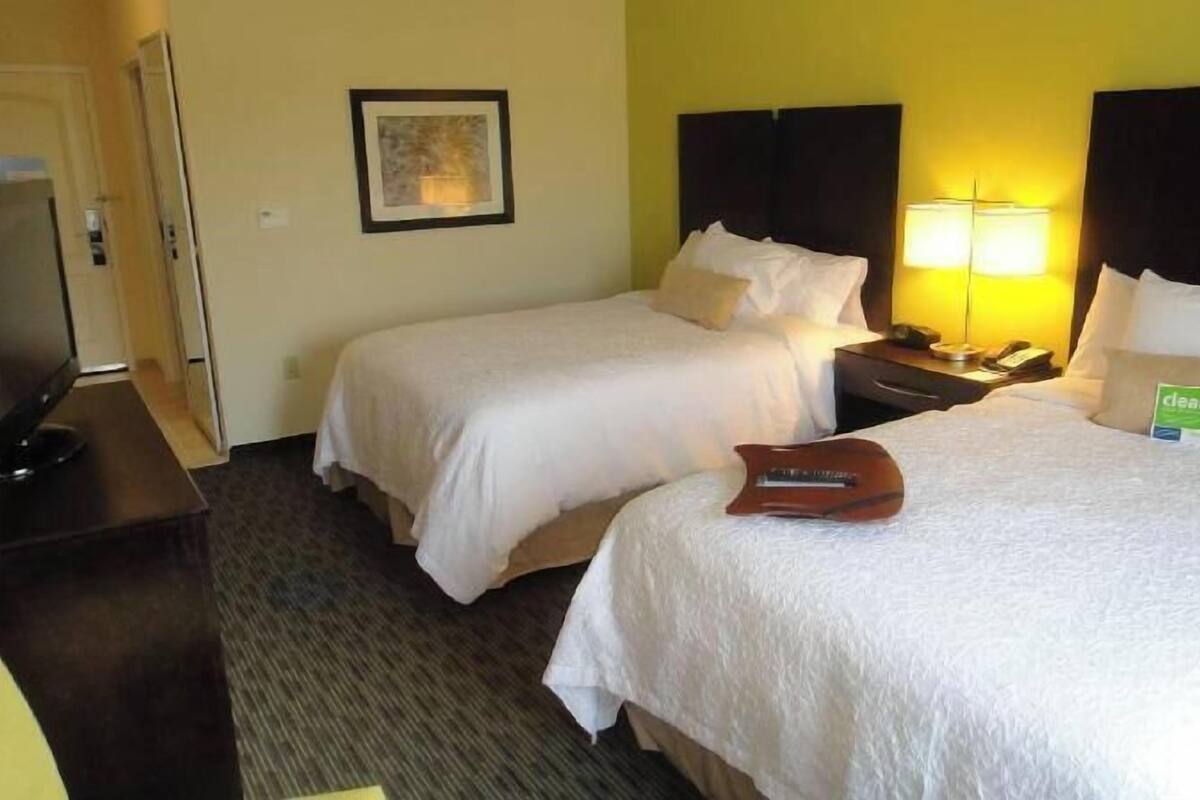 A hotel room with two beds, a desk with a computer, a lamp, and a framed picture on the wall.