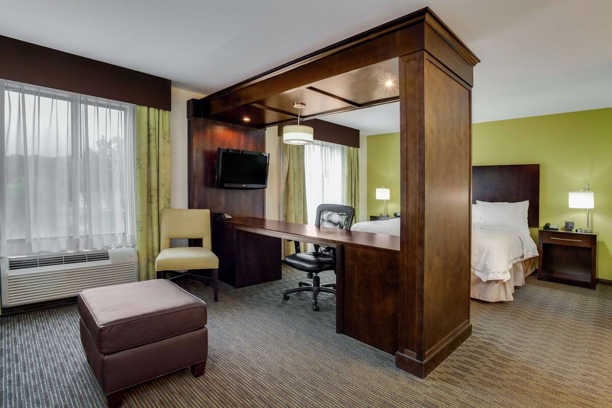 A hotel room with a desk, chair, bed, and a TV.
