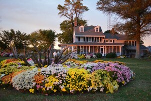 A large house with a porch and a garden with colorful flowers.