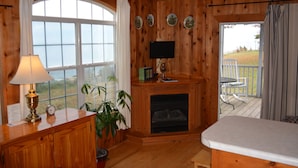 A wooden cabin interior with a fireplace, a television mounted above it, a dining area with a table and chairs, and a large window with curtains. - Black Walnut Point Inn (Tilghman)