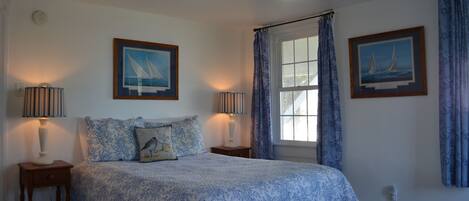 A bedroom with a bed, two bedside tables, a ceiling fan, and two framed pictures on the walls.