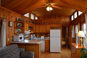 A wooden cabin interior with a kitchen, dining area, and a ceiling fan.