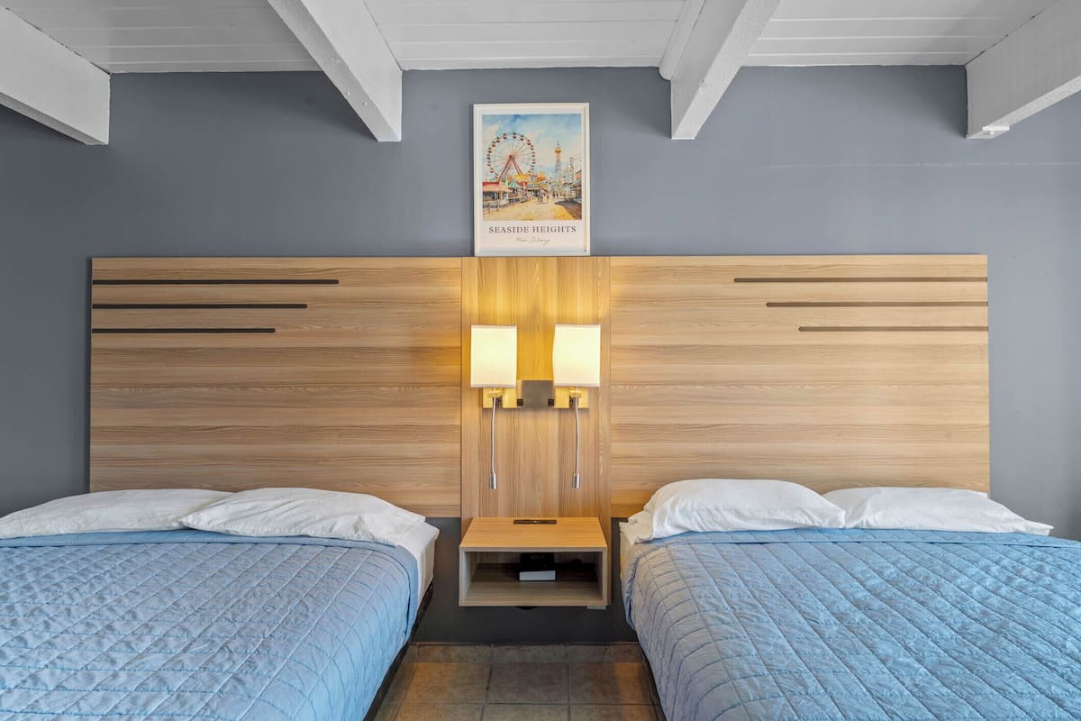 A hotel room with two beds, a wooden headboard, bedside lamps, a framed picture on the wall, and a small wooden nightstand.
