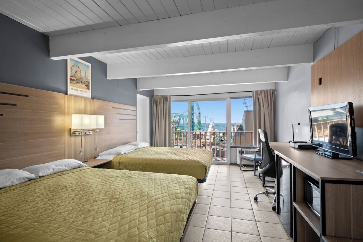 A hotel room with two beds, a desk with a computer, a TV, and a balcony with a view of a Ferris wheel.