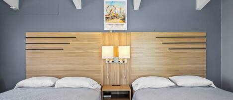 Habitación doble con dos camas, cabecero de madera, lámparas de noche y un póster en la pared.