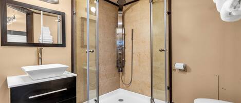 Un baño moderno con ducha de vidrio, un lavabo blanco con espejo y un inodoro.