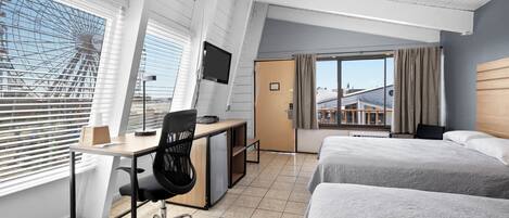 A hotel room with a desk, chair, two beds, a TV, and a large window with blinds.