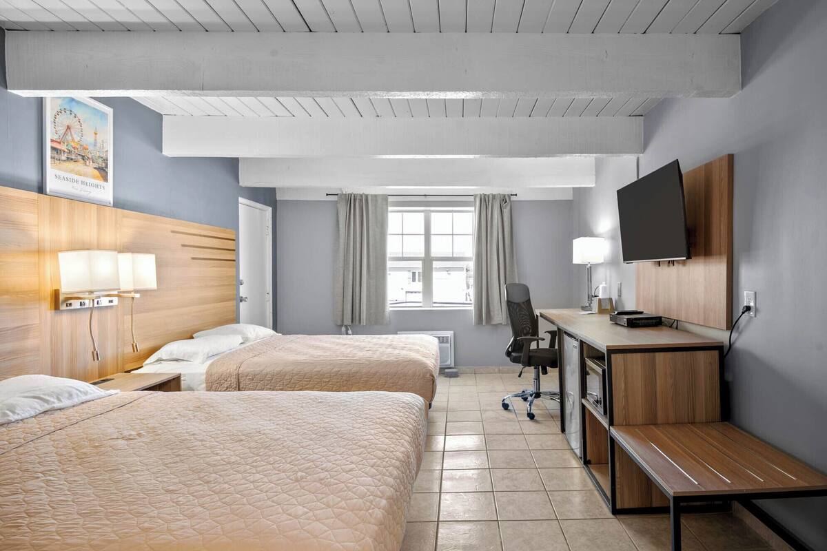 A hotel room with two beds, a desk, a chair, a TV, and a window with curtains.