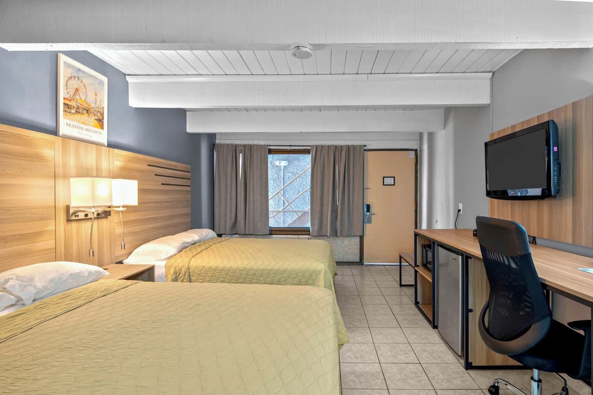 A hotel room with two beds, a desk, a chair, a TV, and a window with curtains.
