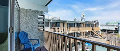 A balcony with a blue chair, a pool, and a building with multiple floors and a staircase.