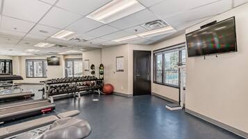 A gym with exercise equipment, a television, and large windows.