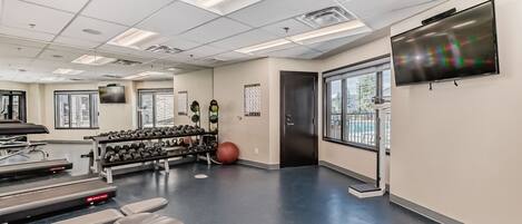 Une salle de sport équipée de matériel d’exercice, d’un téléviseur et dotée de grandes fenêtres.