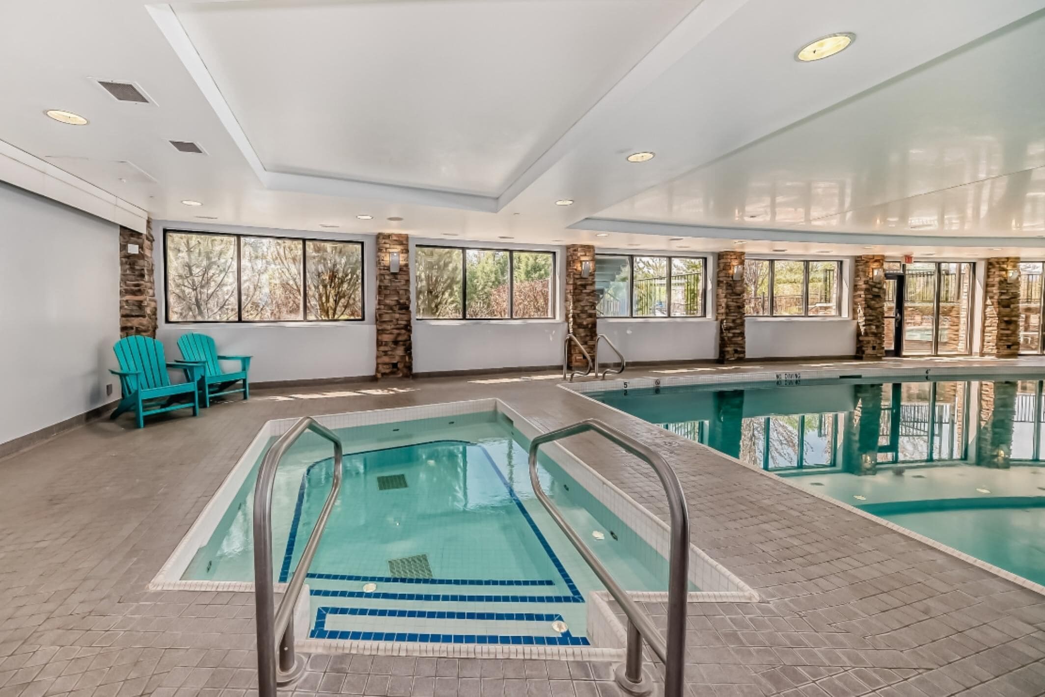 Una piscina interior con agua azul cristalina, pilares de piedra y amplios ventanales.