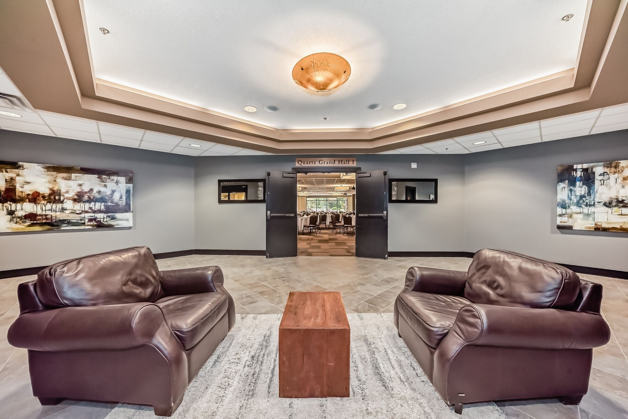 Un hall d’entrée avec deux canapés en cuir, une table basse en bois et un panneau indiquant « Quartz Grand Hall 1 ».