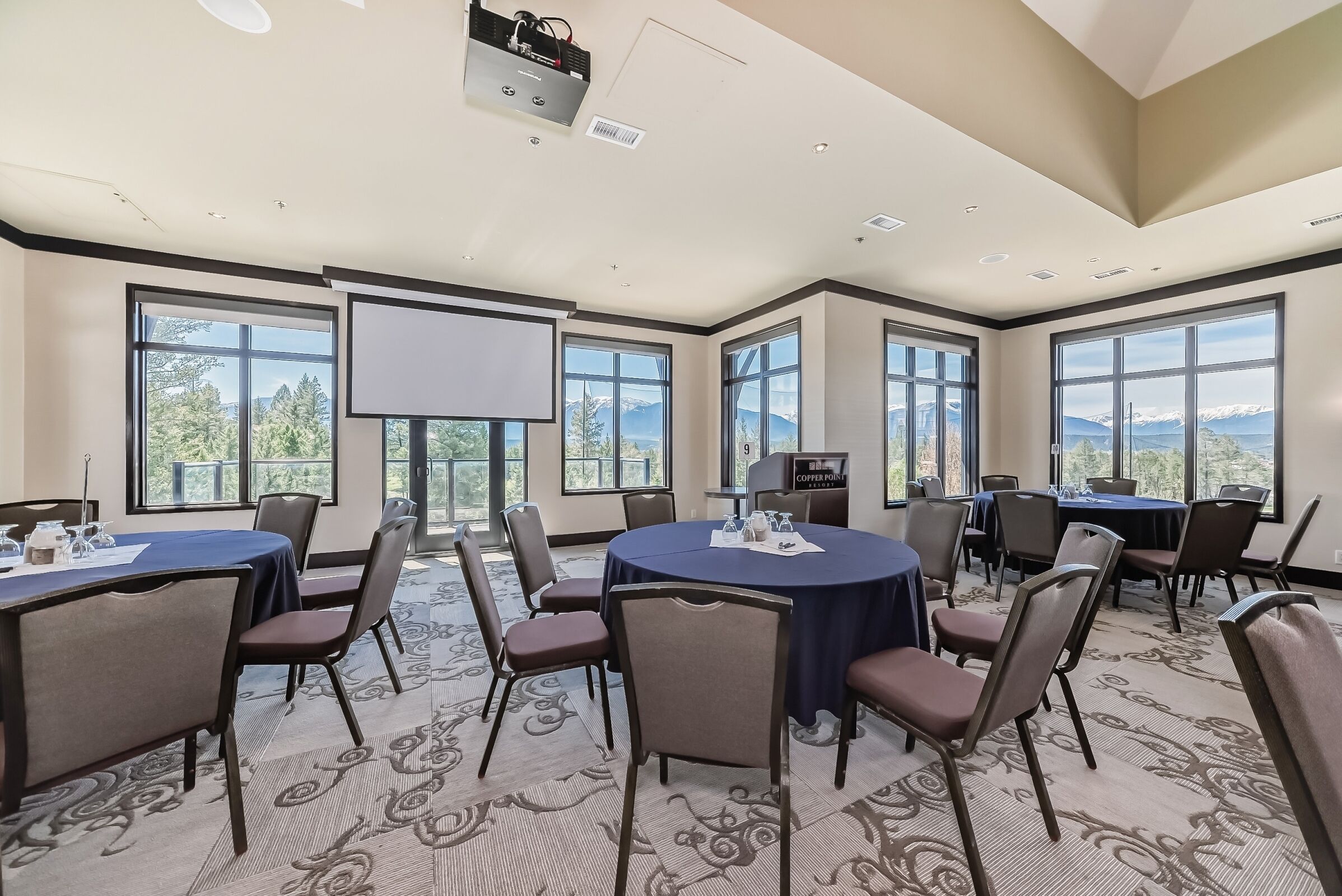 A conference room with large windows, a projector, and a table with chairs.