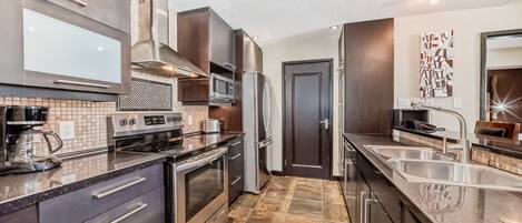 Una cucina moderna con elettrodomestici in acciaio inox, una grande isola con lavello e una porta in legno scuro.