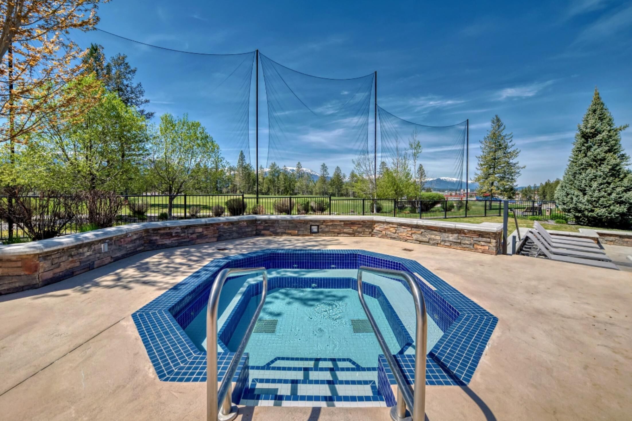 Una piscina con revestimiento de azulejos azules, rodeada por un muro de piedra y barandillas de metal.