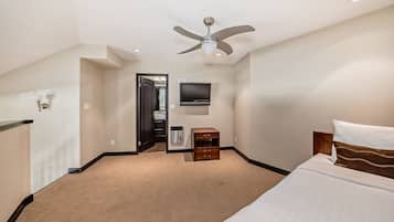 Habitació d'hotel amb un llit, un ventilador de sostre, un televisor, una commode i una porta que dona a un bany.