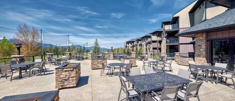 An outdoor patio area with tables and chairs, stone planters, and a view of mountains.