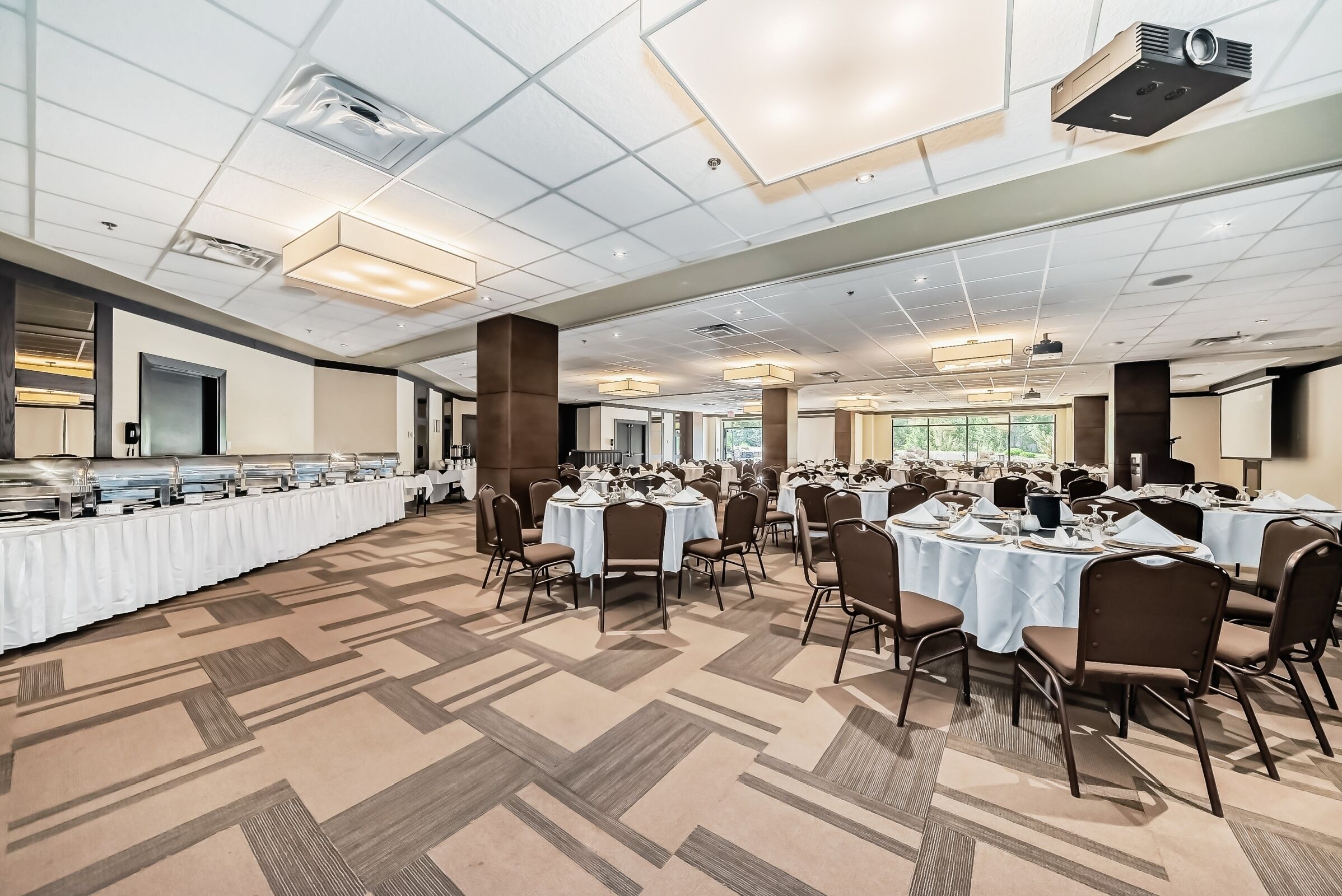 A banquet hall with round tables, chairs, and buffet counters.