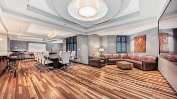 A modern conference room with a wooden parquet floor, leather sofas, and a large table with chairs.