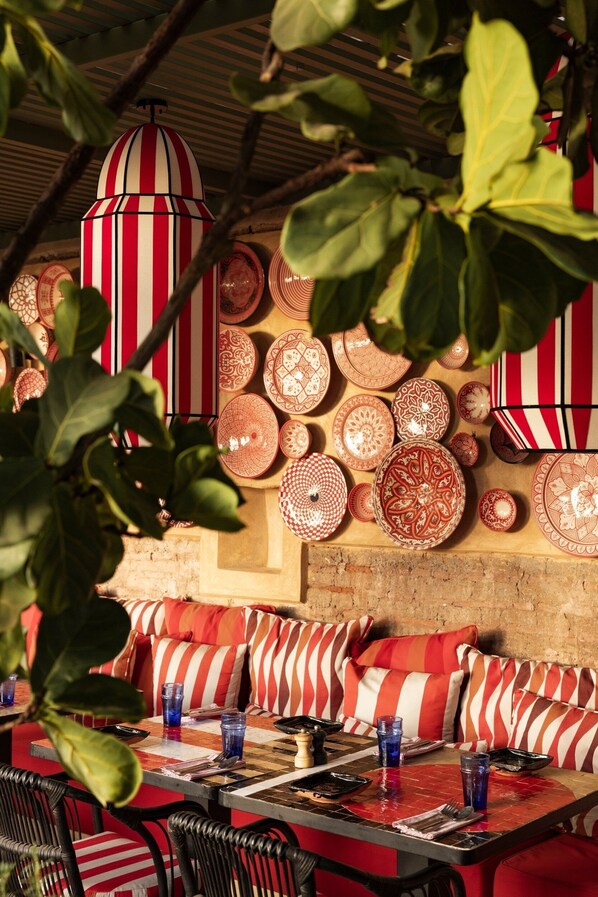 A restaurant with striped red and white cushions, a variety of patterned plates on the wall, and hanging red and white striped lamps. - El Fenn (Marrakech)