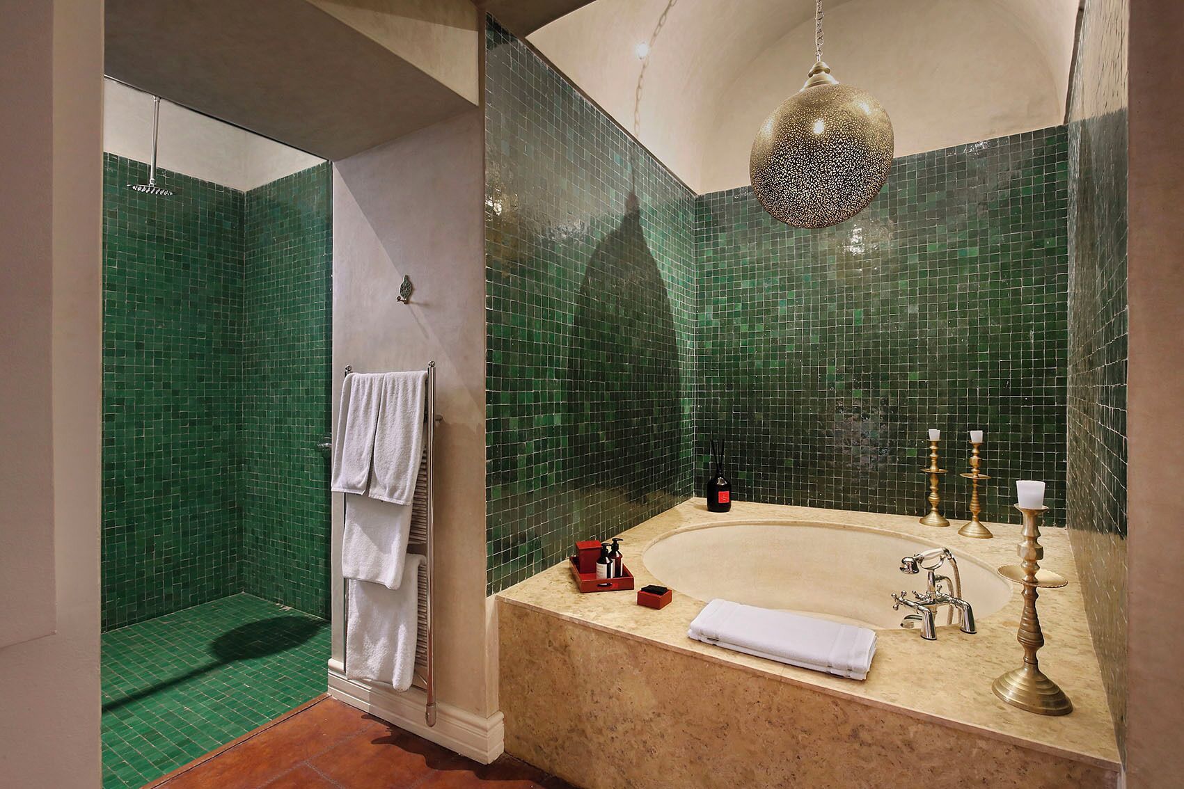 Een badkamer met een douche in groene tegels, een badkuip in beige kleur met gouden details, en een hangende lamp.