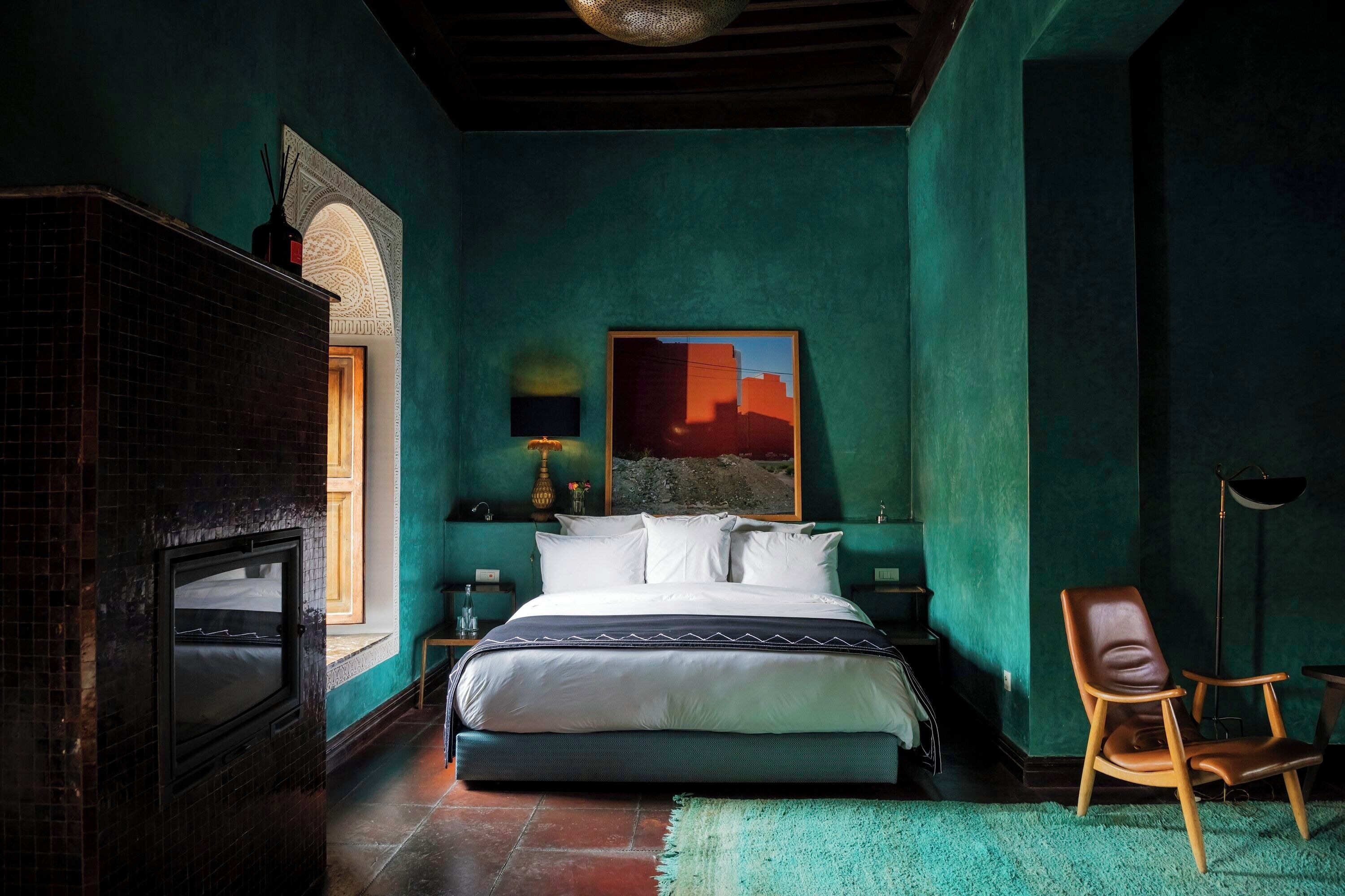 Un dormitorio con una cama grande, una chimenea, una silla y un cuadro en la pared.