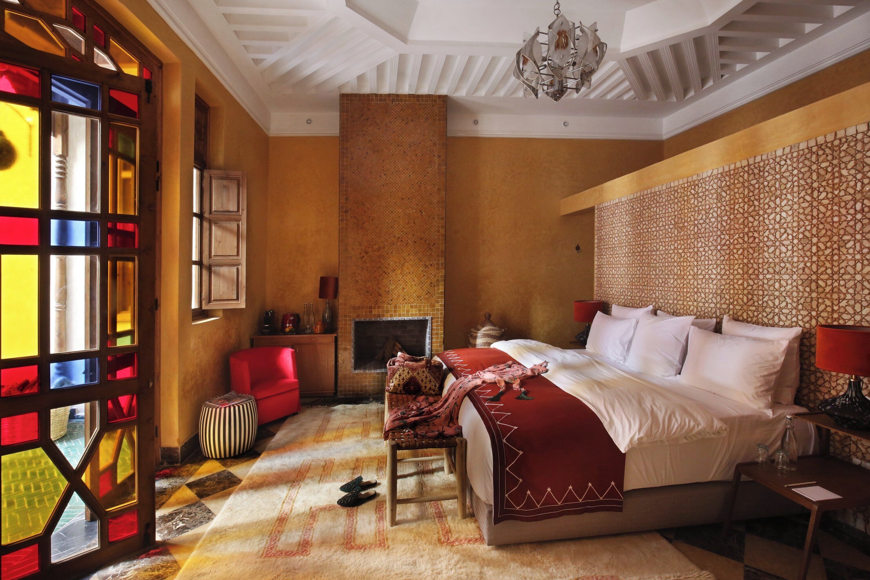 A hotel room with a large bed, a red sofa, a patterned wall, and a fireplace.