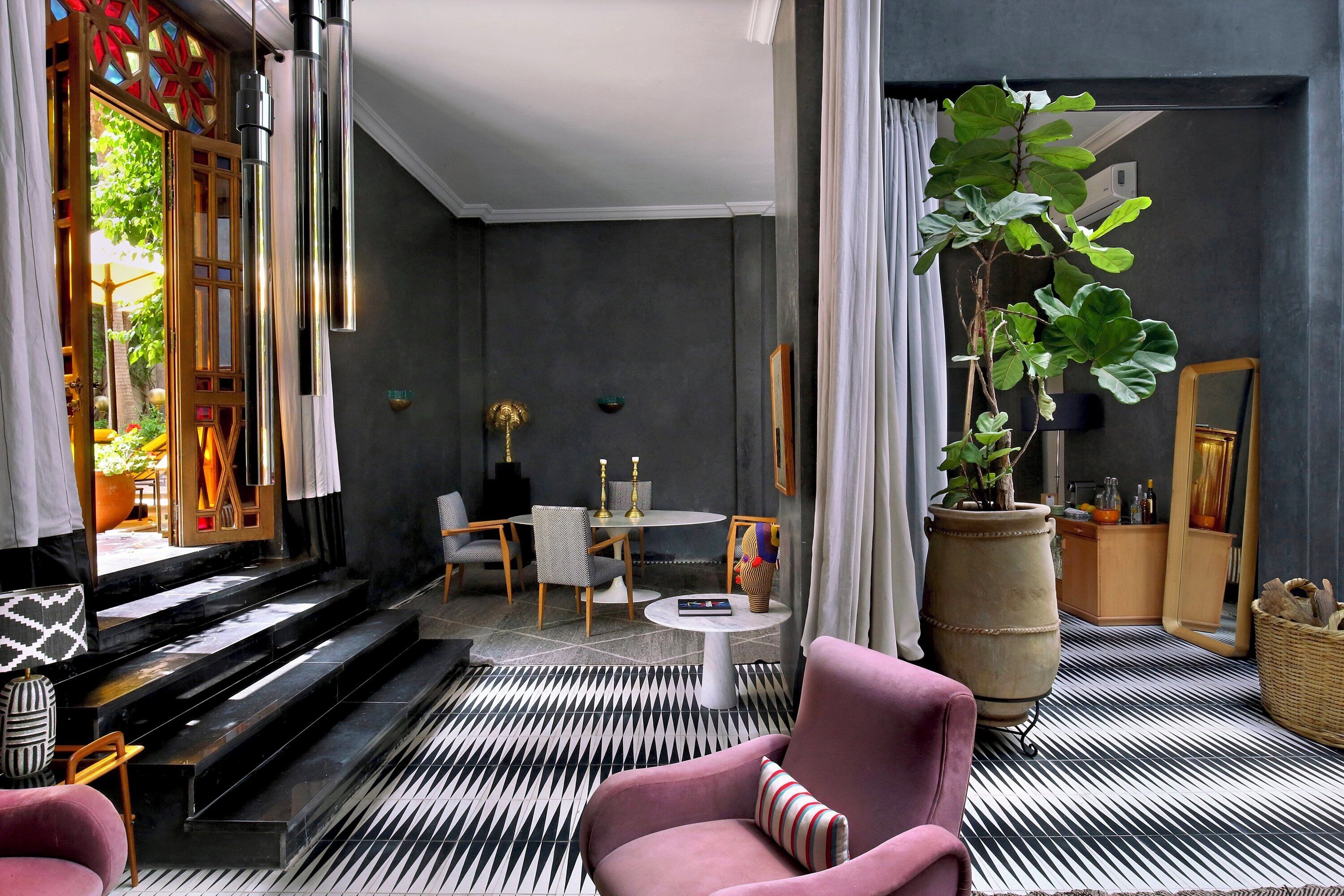 A modern interior with a black and white patterned floor, a pink armchair, a large potted plant, and a dining area with a round table and chairs.