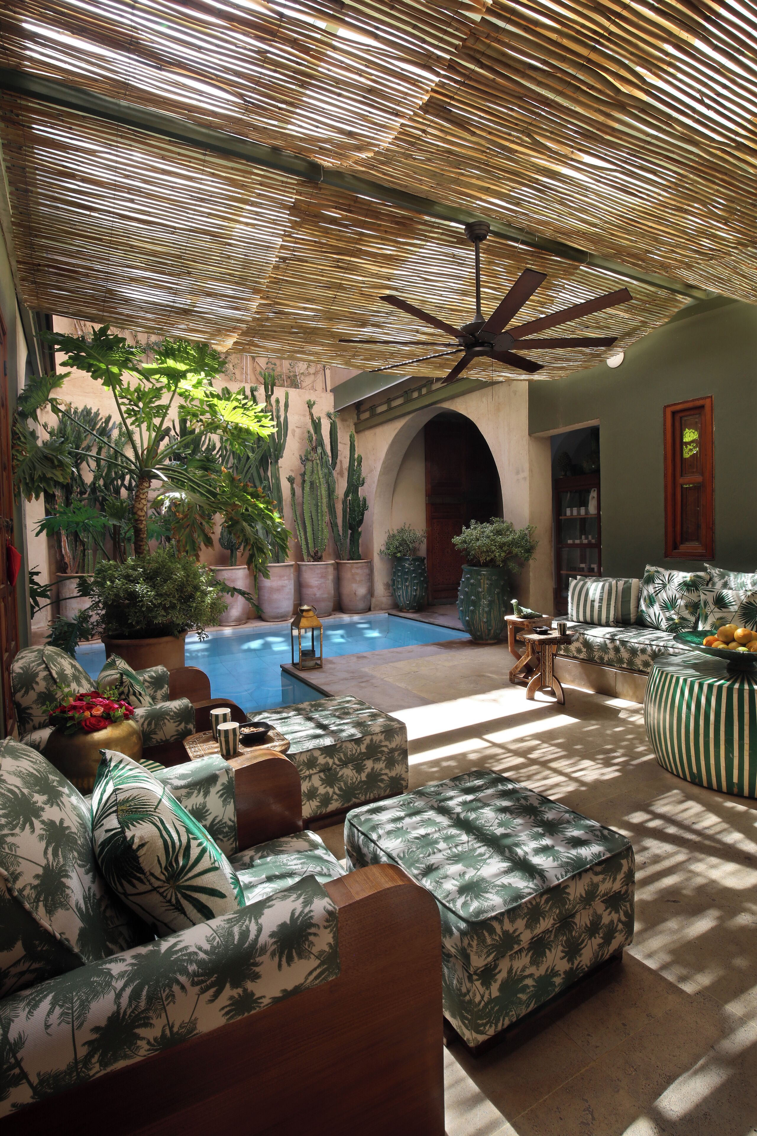 A sunlit indoor space with a pool, seating areas, and various potted plants.