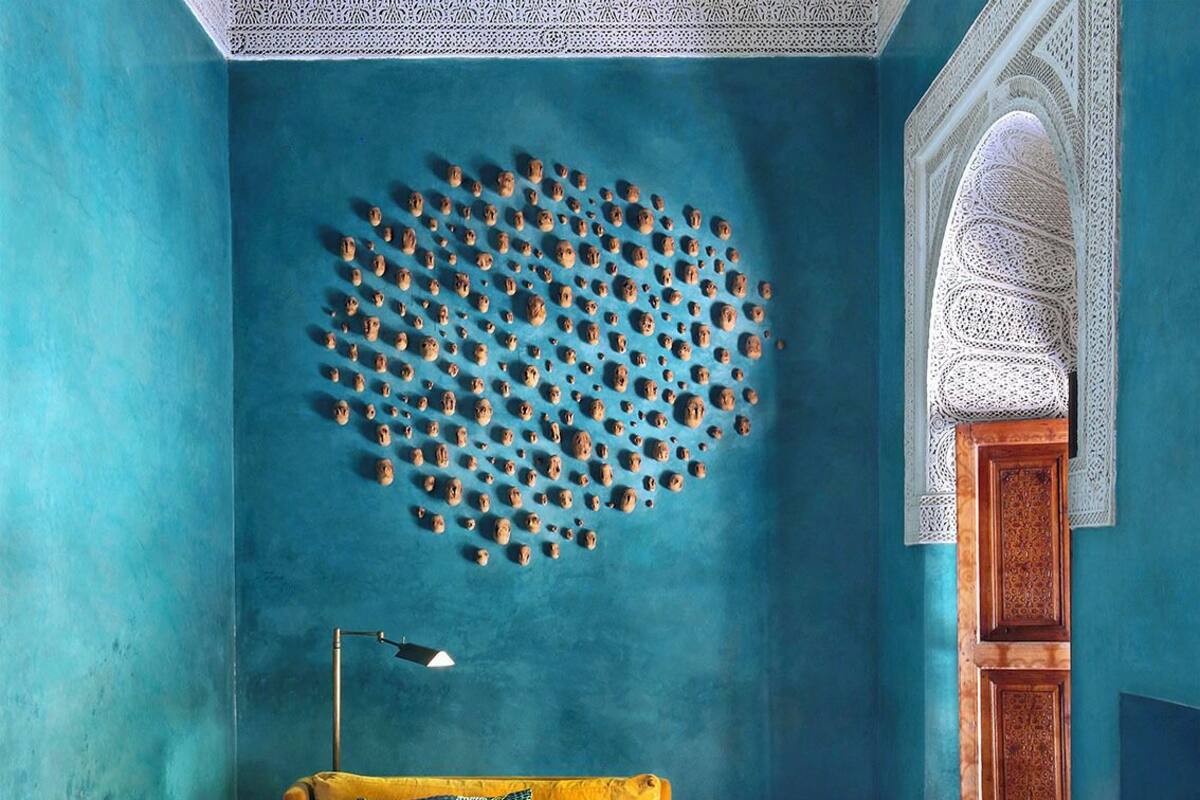 A room with a blue wall, a geometric wall art, a yellow sofa, a black and white checkered floor, and a traditional archway.