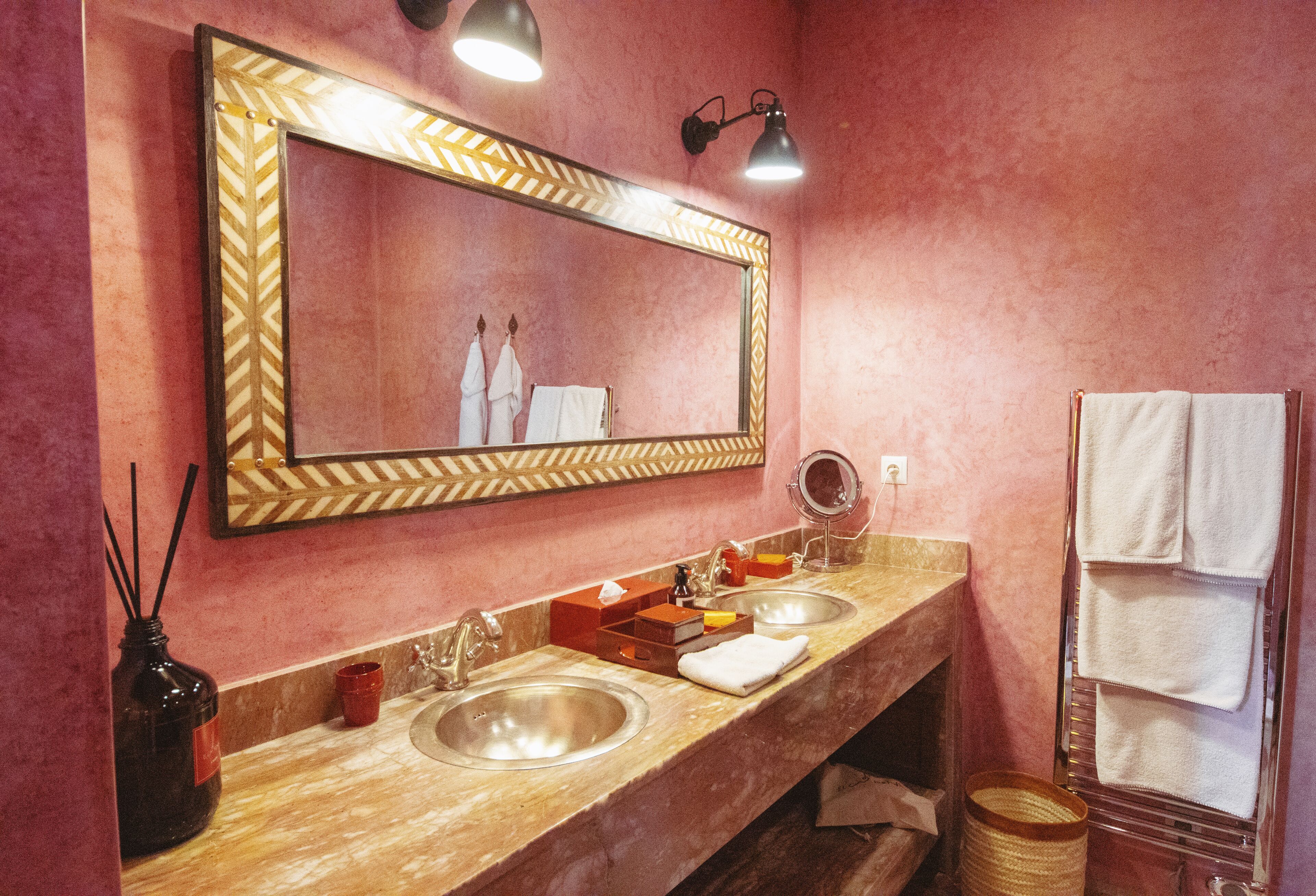 A bathroom with a large mirror, two sinks, a vanity, and a towel rack.