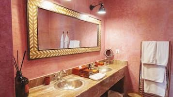 A bathroom with a large mirror, two sinks, a vanity, and a towel rack.