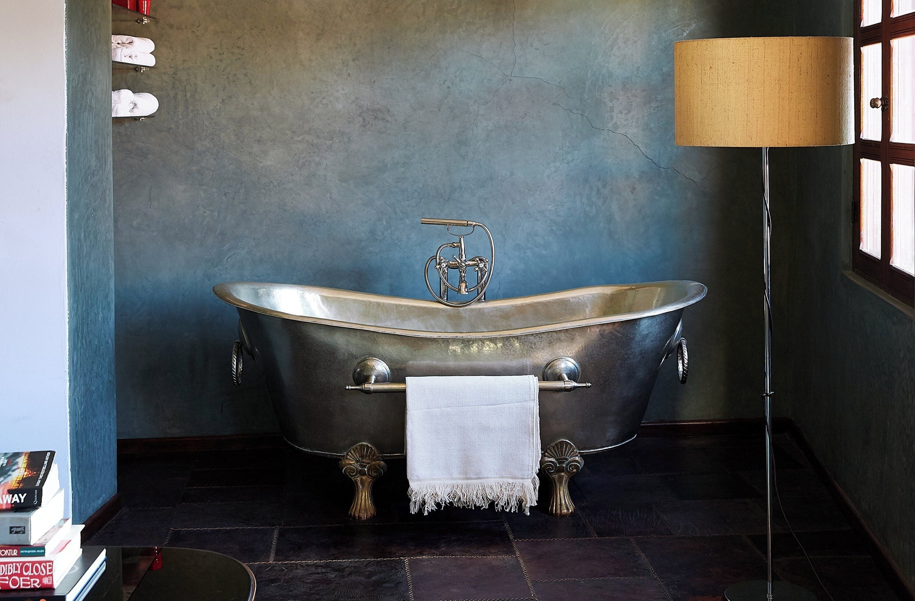A vintage-style bathtub with a towel, a floor lamp, and a window with wooden frames.