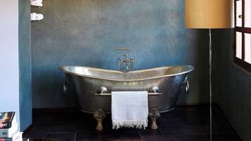 A vintage-style bathtub with a towel, a floor lamp, and a window with wooden frames.