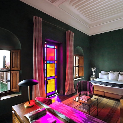 A hotel room with a bed, a chair, a desk, and a window with curtains.