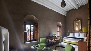 A room with a bed, a desk, a chair, and a sofa. There are windows with curtains and a lamp on the desk.
